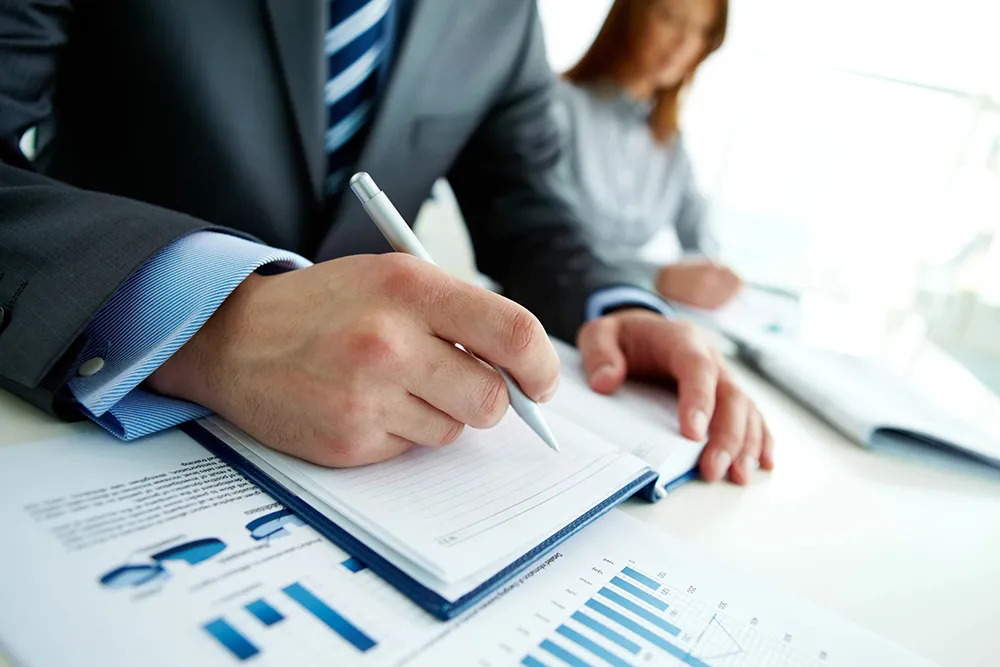 Unrecognizable business person analyzing graphs and taking notes