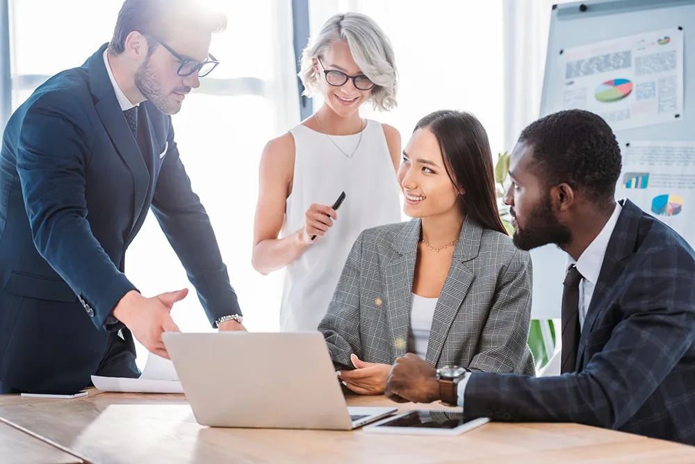 Smiling multiethnic businesspeople working on project in office and looking at laptop