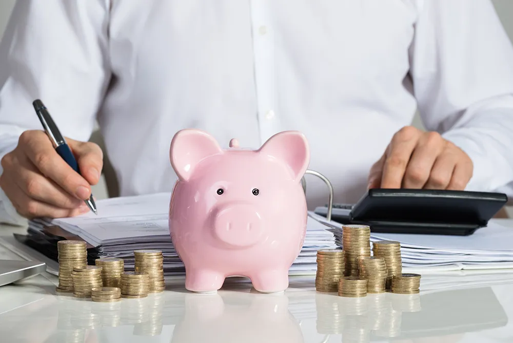 Midsection of businessman calculating invoice with piggybank and coins at office desk